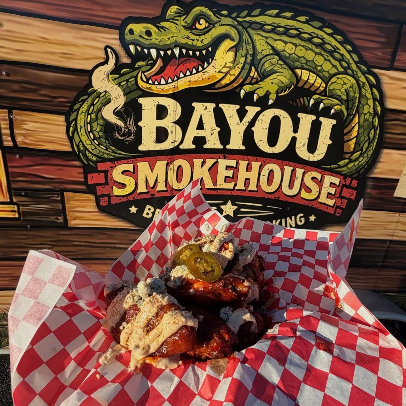 Smoked wings on red-checkered paper under the Bayou Smokehouse sign
